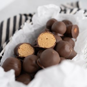 Close up of one chocolate covered peanut butter ball cut in half in a bowl with additional balls.