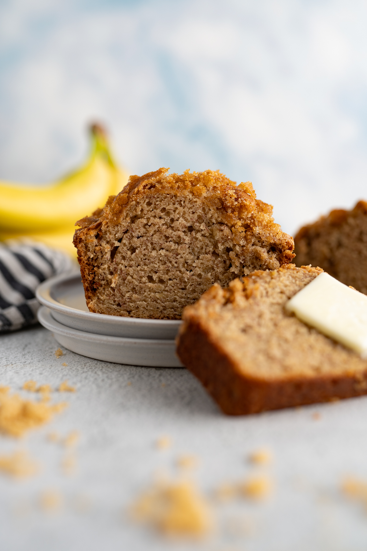 A loaf of moist banana bread cut on a plate with a slice leaning against it.