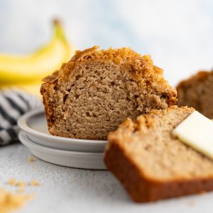 A loaf of moist banana bread cut on a plate with a slice leaning against it.
