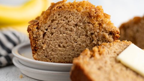 A loaf of moist banana bread cut on a plate with a slice leaning against it.