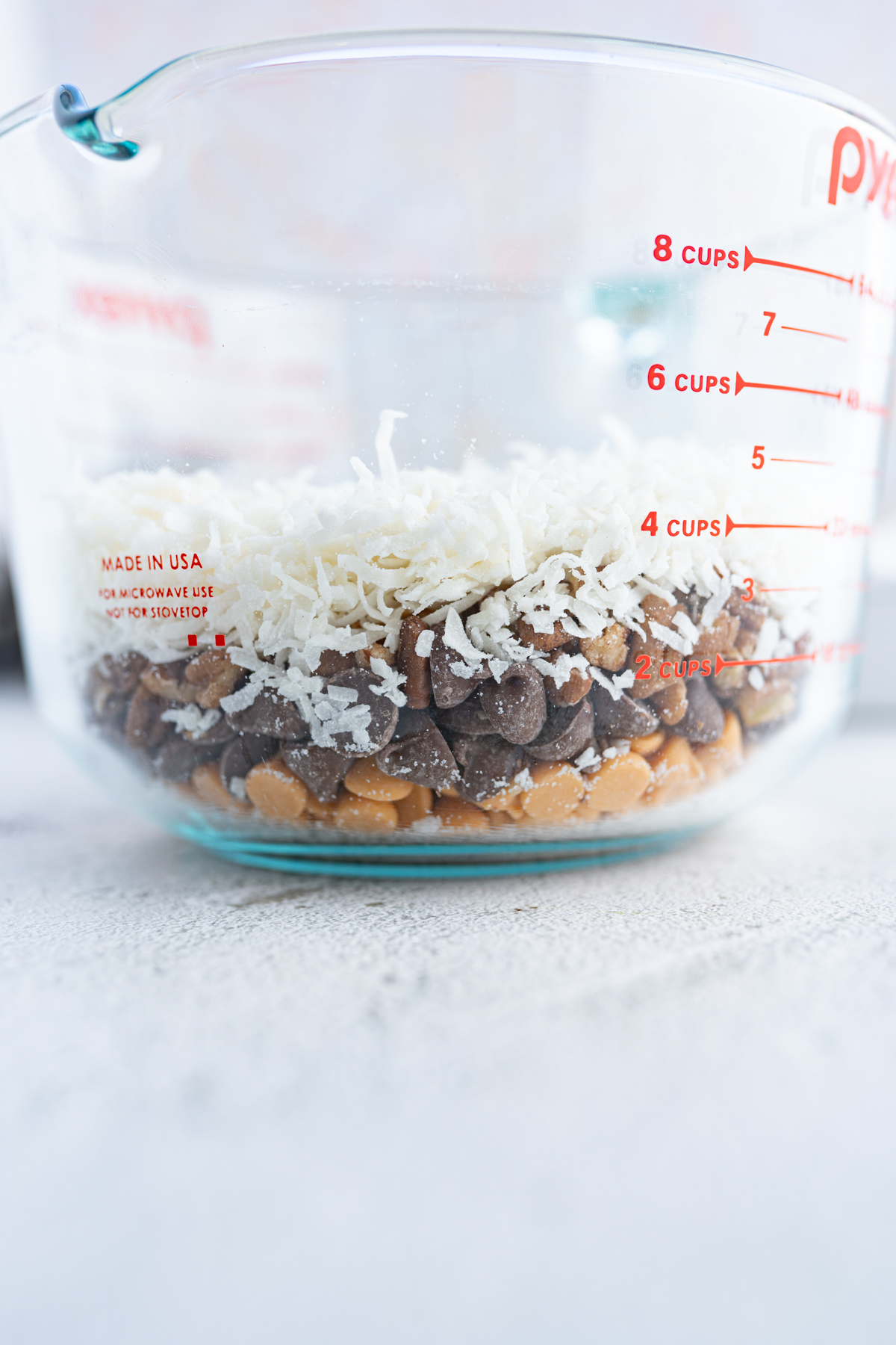 A clear bowl of coconut, chocolate chips, butterscotch chips and pecans to be added to magic cookie bars. 
