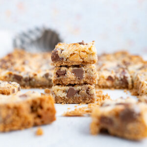 A stack of 7 layer magic cookie bars on the counter surrounded by additional bars.