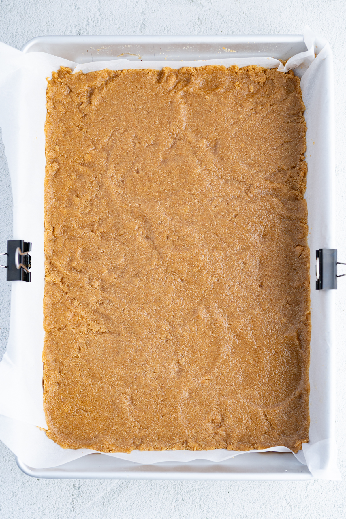 Graham cracker butter mixture pressed into the bottom of a pan for magic cookie bars. 