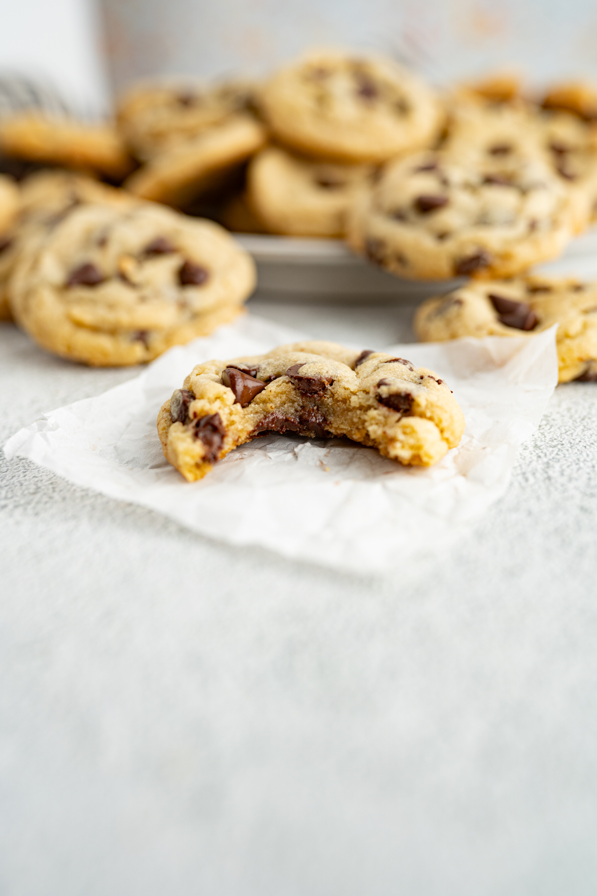 A single soft and chewy chocolate chip cookie with a bite out of it on a parchment paper piece. 