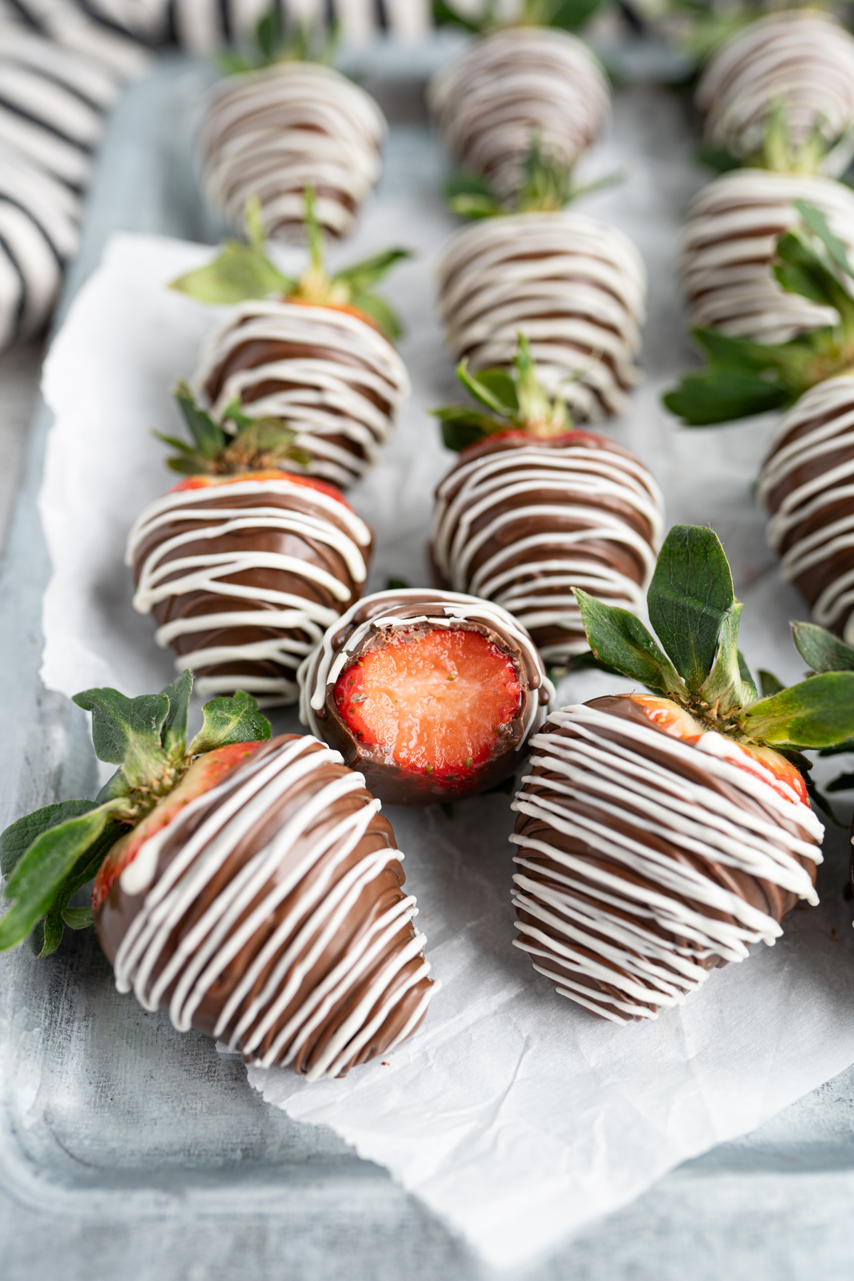 Chocolate dipped strawberries lined up on a tray with one half eaten on top. 