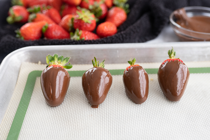 4 glossy chocolate strawberries on a parchment lined sheet after being dipped. 