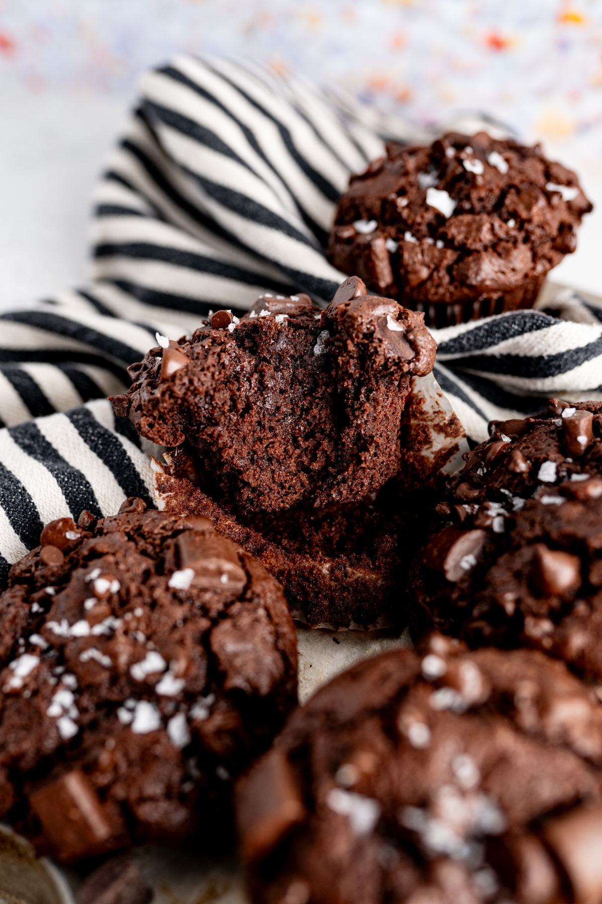 A pile of chocolate chocolate muffins with one muffin with a bite out of it. 