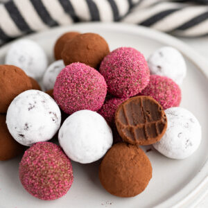 A plate of multi-colored chocolate truffles. One has a bite out of it.