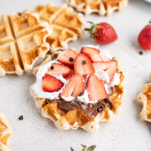 Close up of a liege waffle (waffle love copycat) topped with strawberries, cream and chocolate.