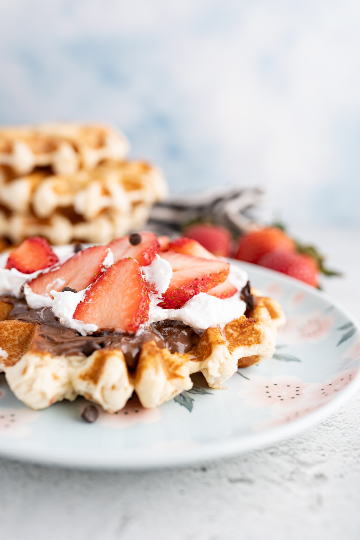 Side view of a liege waffle with chocolate, berries and cream topping it. 