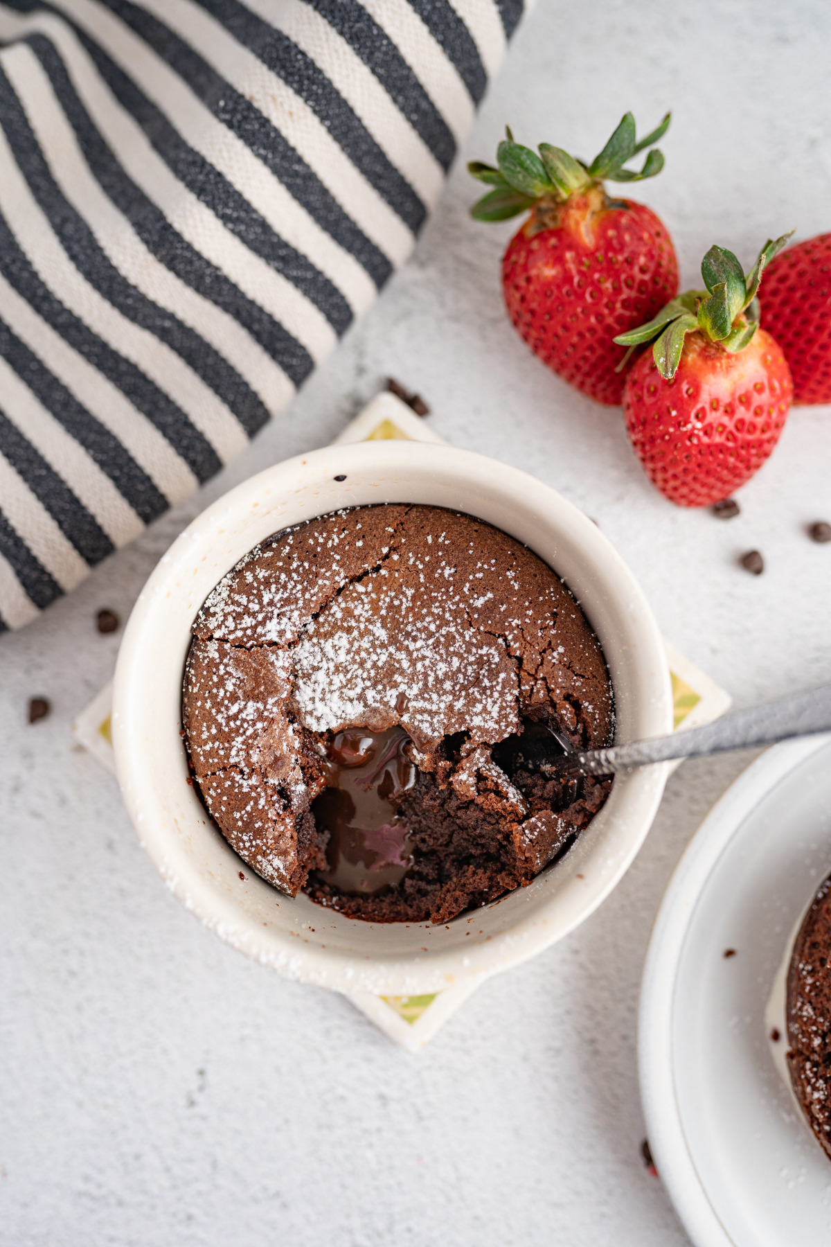 Aerial image of a chocolate lava cake in a ramekin with a spoon sticking out of it. 