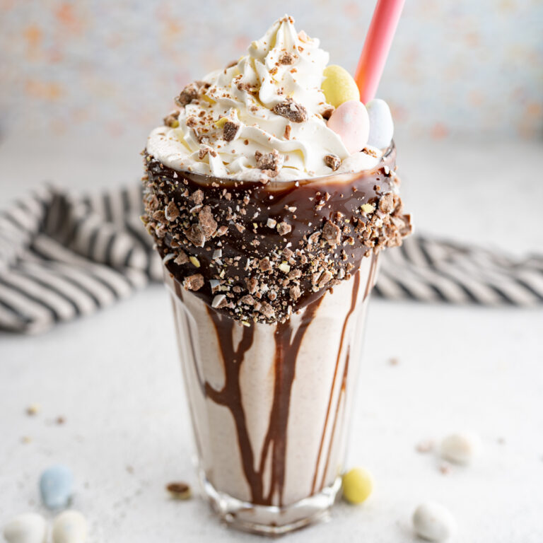 A cadbury egg milkshake with hot fudge streaming down the side of the glass and topped with whipped cream.