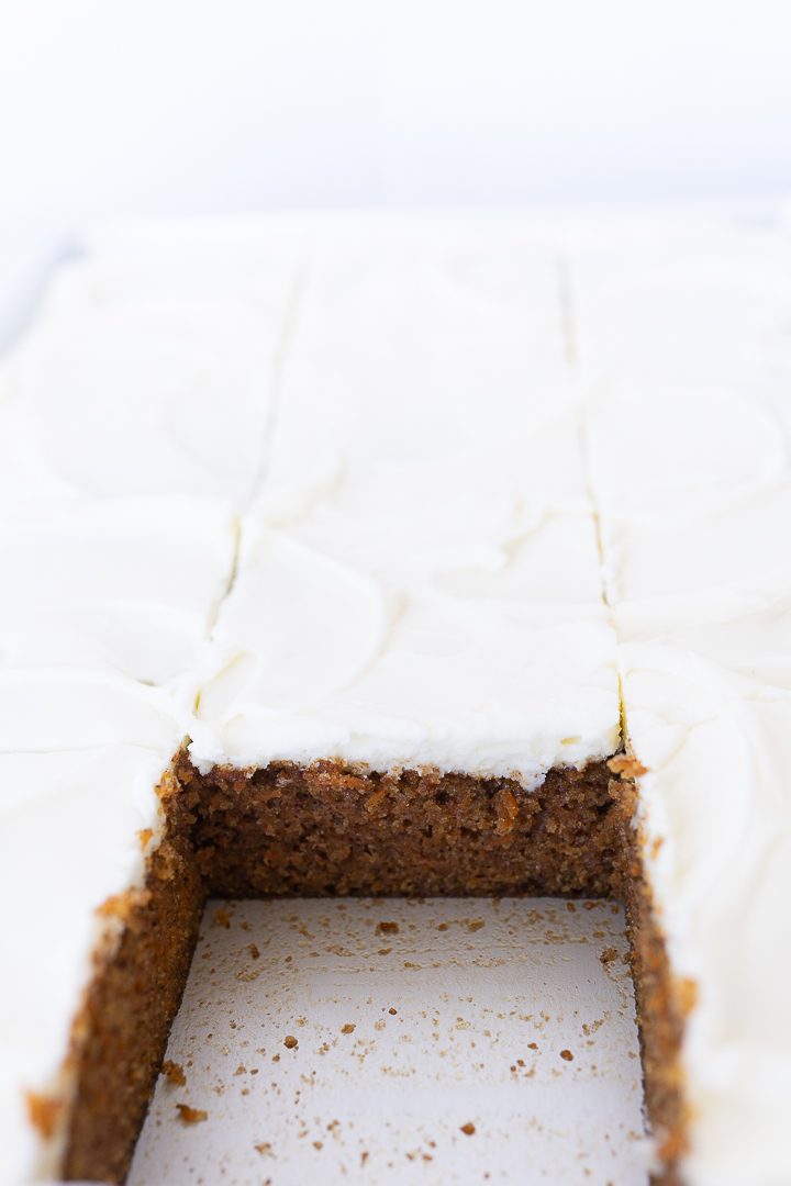 Side view of a sheet pan of carrot cake cut into squares. One of the squares has been removed. 