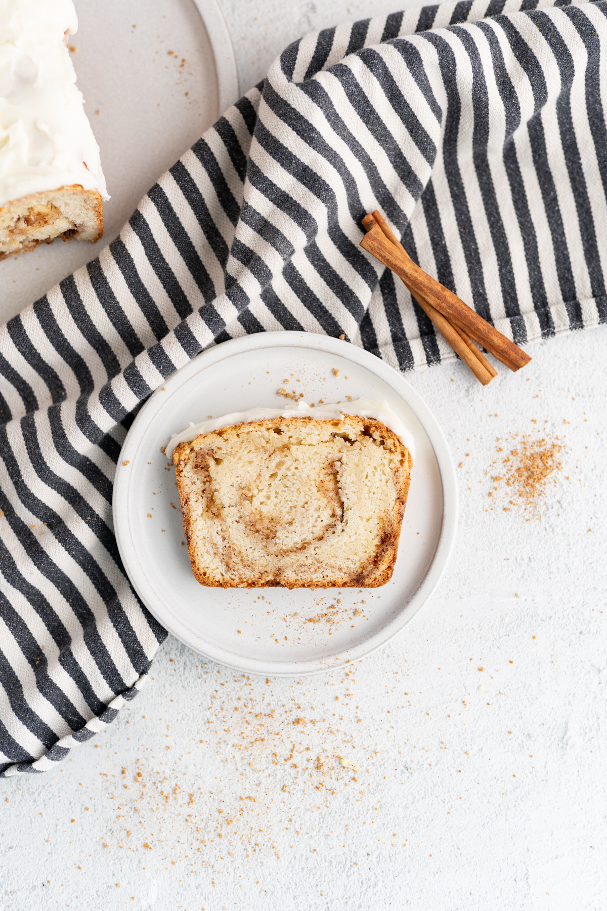 A slice of cinnamon swirl bread on a plate on the counter next to a cinnamon stick. 