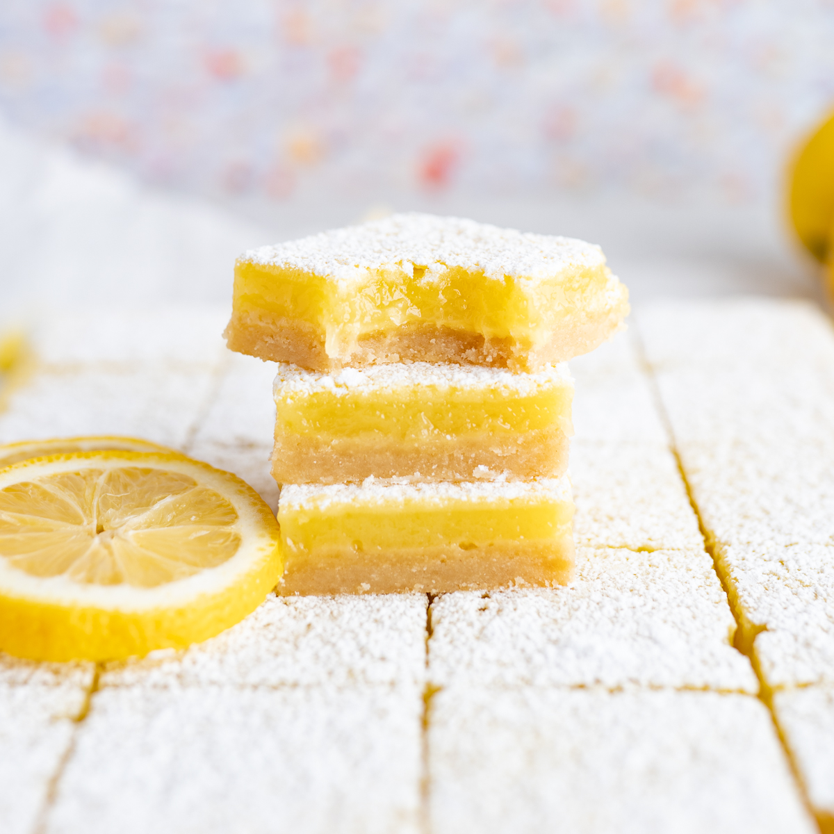3 lemon bars stacked on top of each other next to a lemon slice.