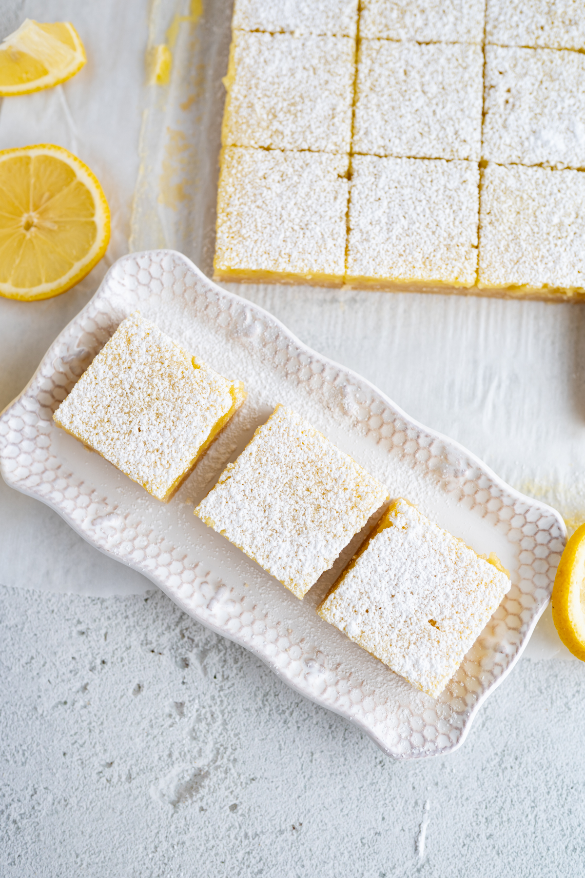 Aerial view of 3 lemon squares on a platter next to a grid of bars.