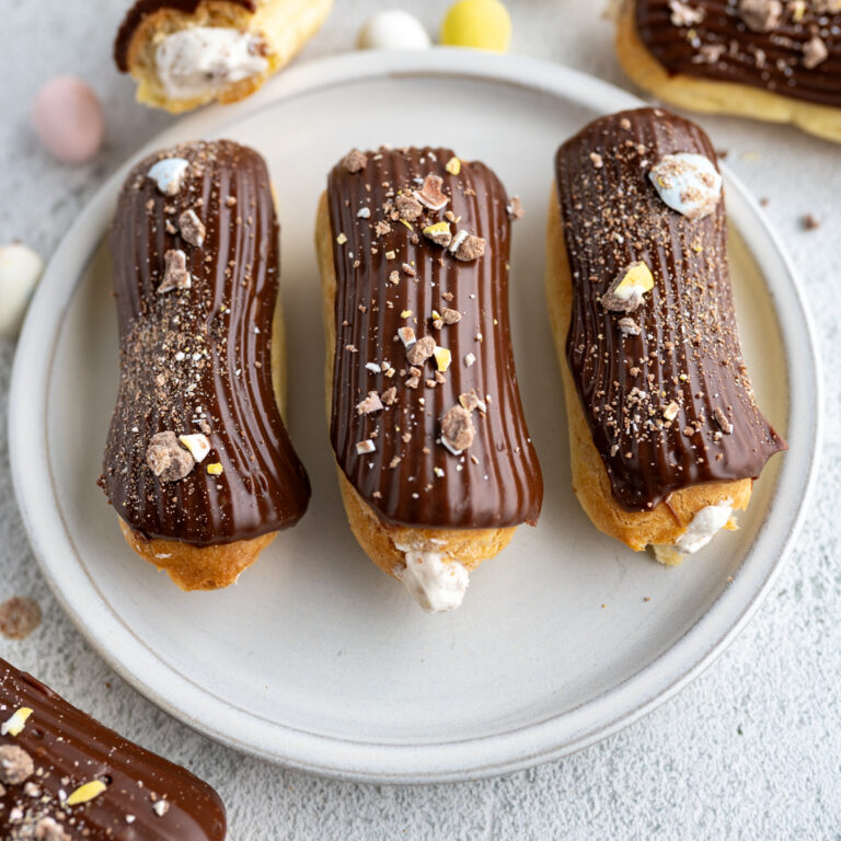 3 chocolate eclairs with cadbury eggs lined up on a plate.