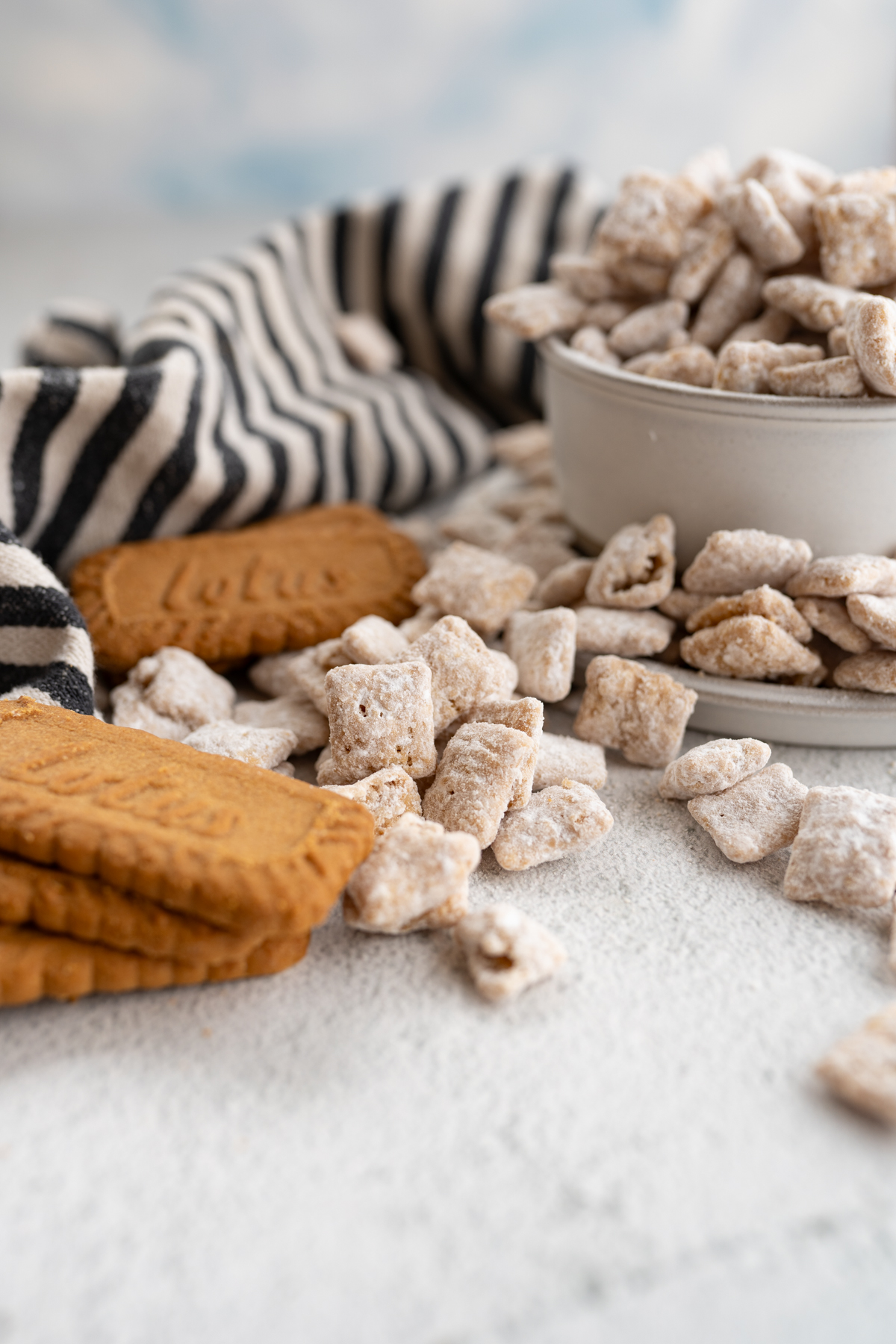 Close up of cookie butter puppy chow spilling onto the counter next to biscoff cookies. 