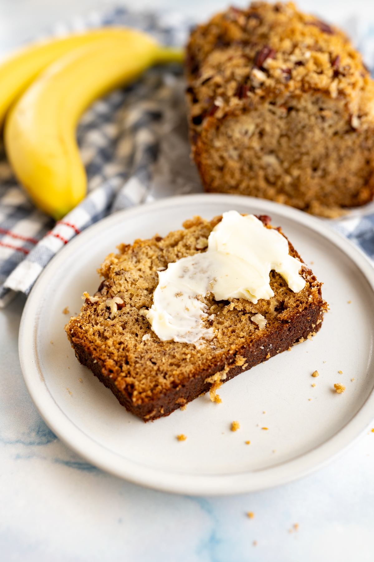 A slice of banana nut bread on a plate with butter. 