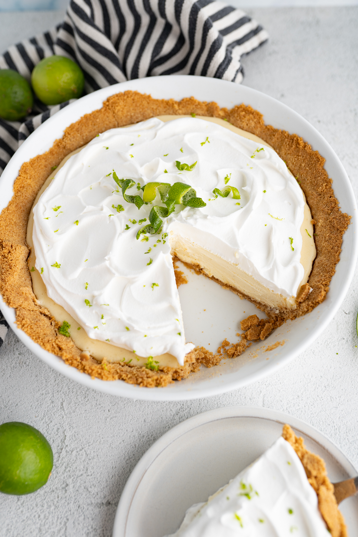 A key lime pie with a slice taken out of it. The slice is on a plate next to the pie. 