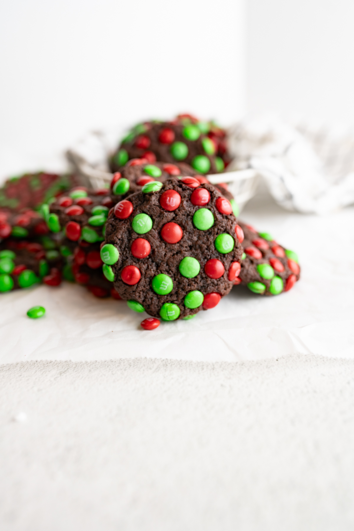 An m&m chocolate cookie propped up by other christmas cookies. 