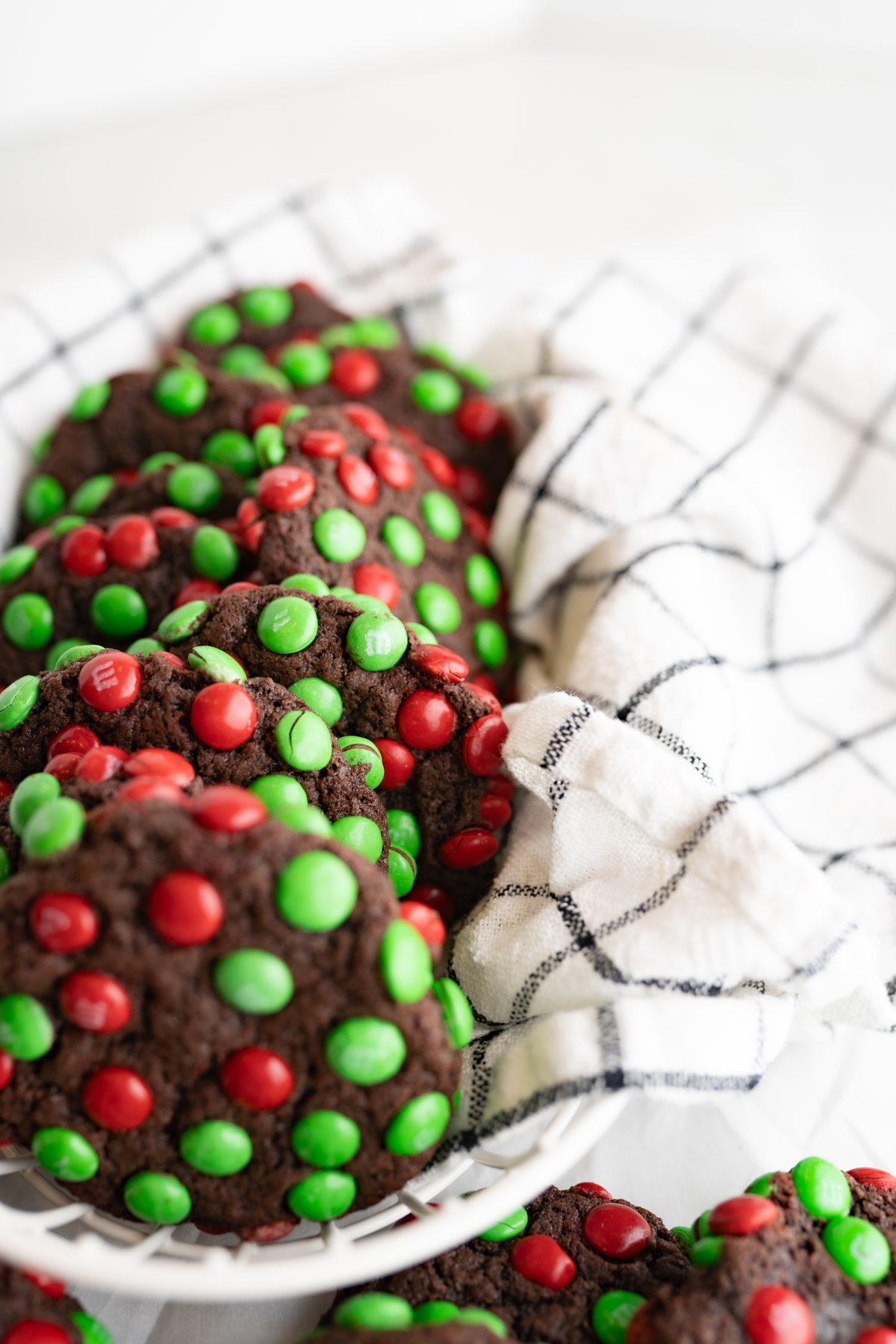 Close up of chocolate cookies covered in Christmas m&ms laying in a basket. 