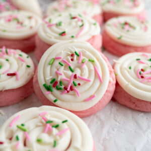 A pink velvet cookie with cream cheese frosting and Christmas sprinkles.