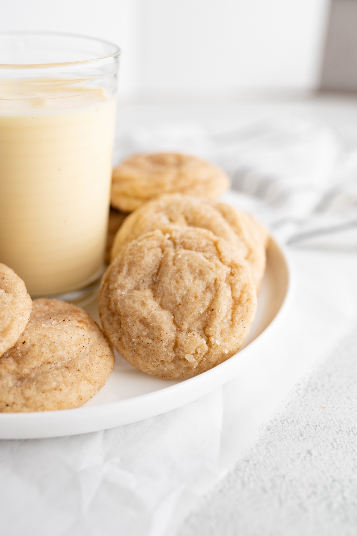 An egg nog snickerdoodle cookie propped on a plate next to a glass of egg nog. 