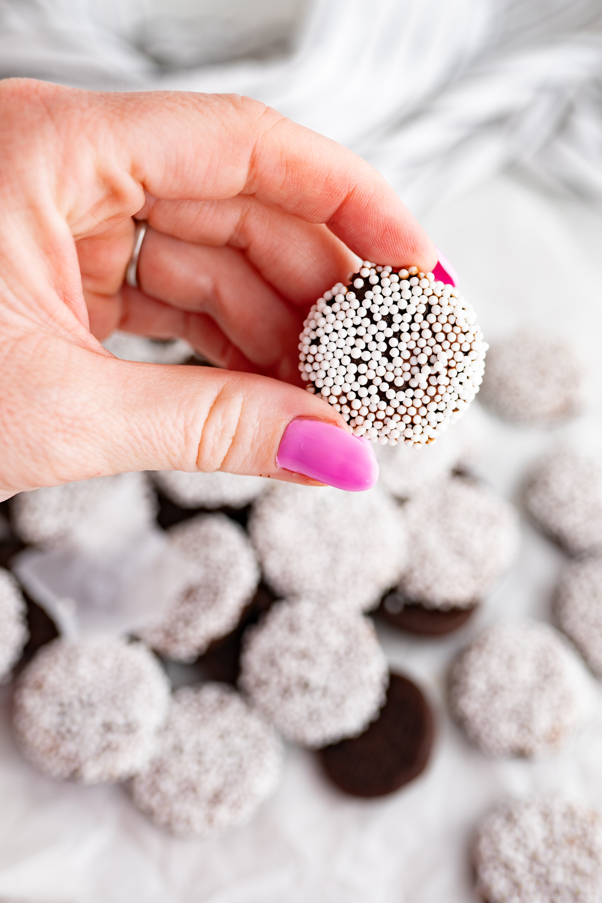 A hand holding up a tiny, one-bite chocolate cookie. 