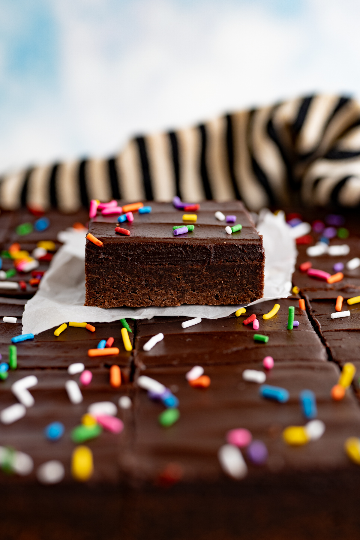 Side view of a single chocolate sugar cookie bar on top of a sheet of other bars. 