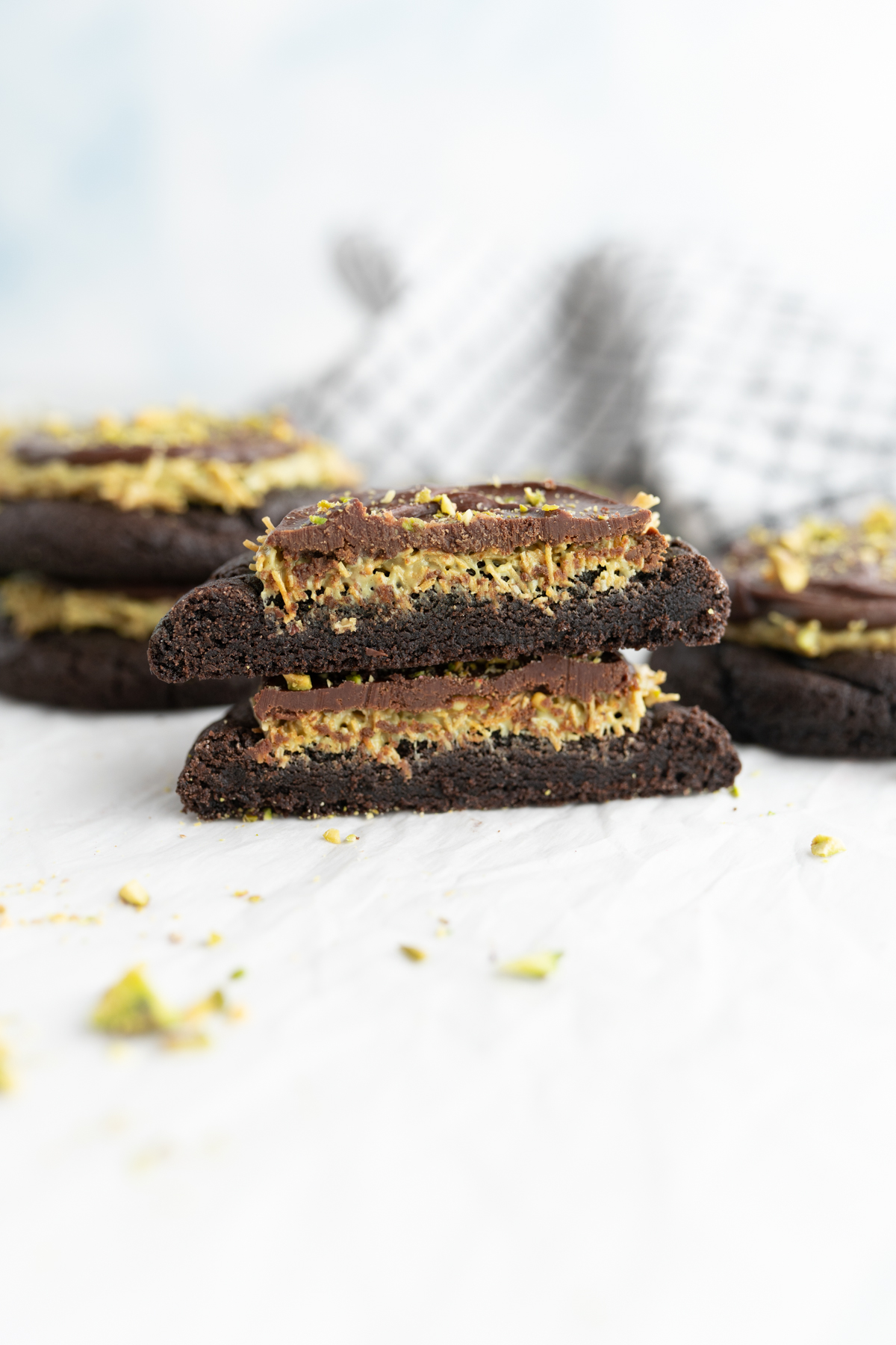 Side view of a chocolate cookie topped with pistachio kataifi, chocolate ganache, and chopped pistachios. 