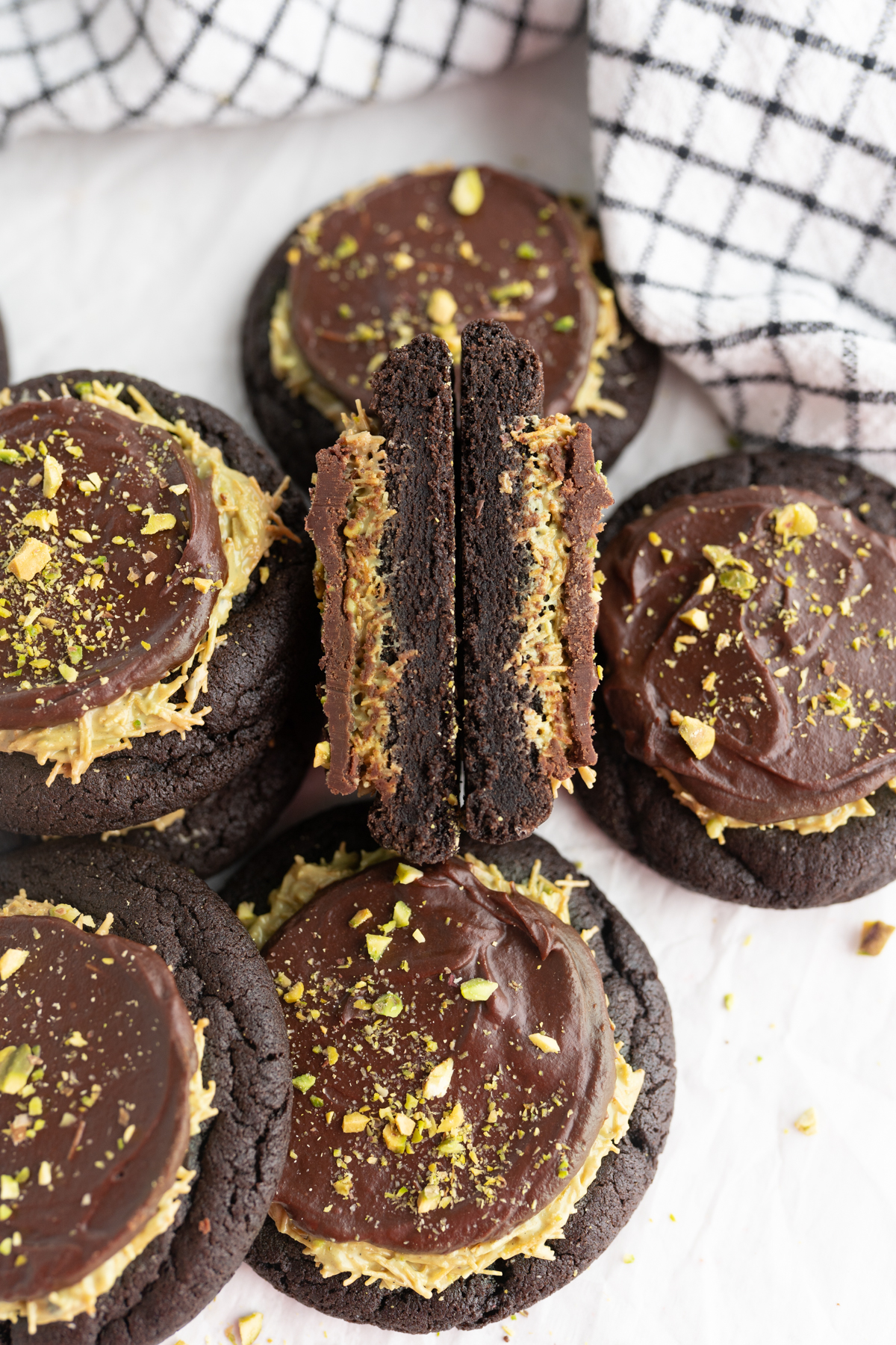 A dubai chocolate cookie cut in half and stacked together to reveal a chocolate cookie, pistachio topping and chocolate ganache. 